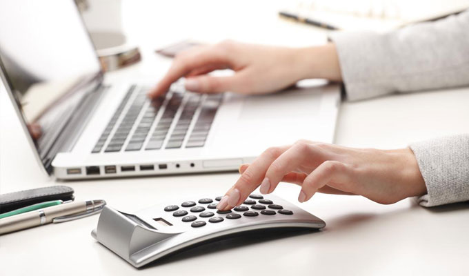 Une femme travaillant sur son laptop et sa calculette